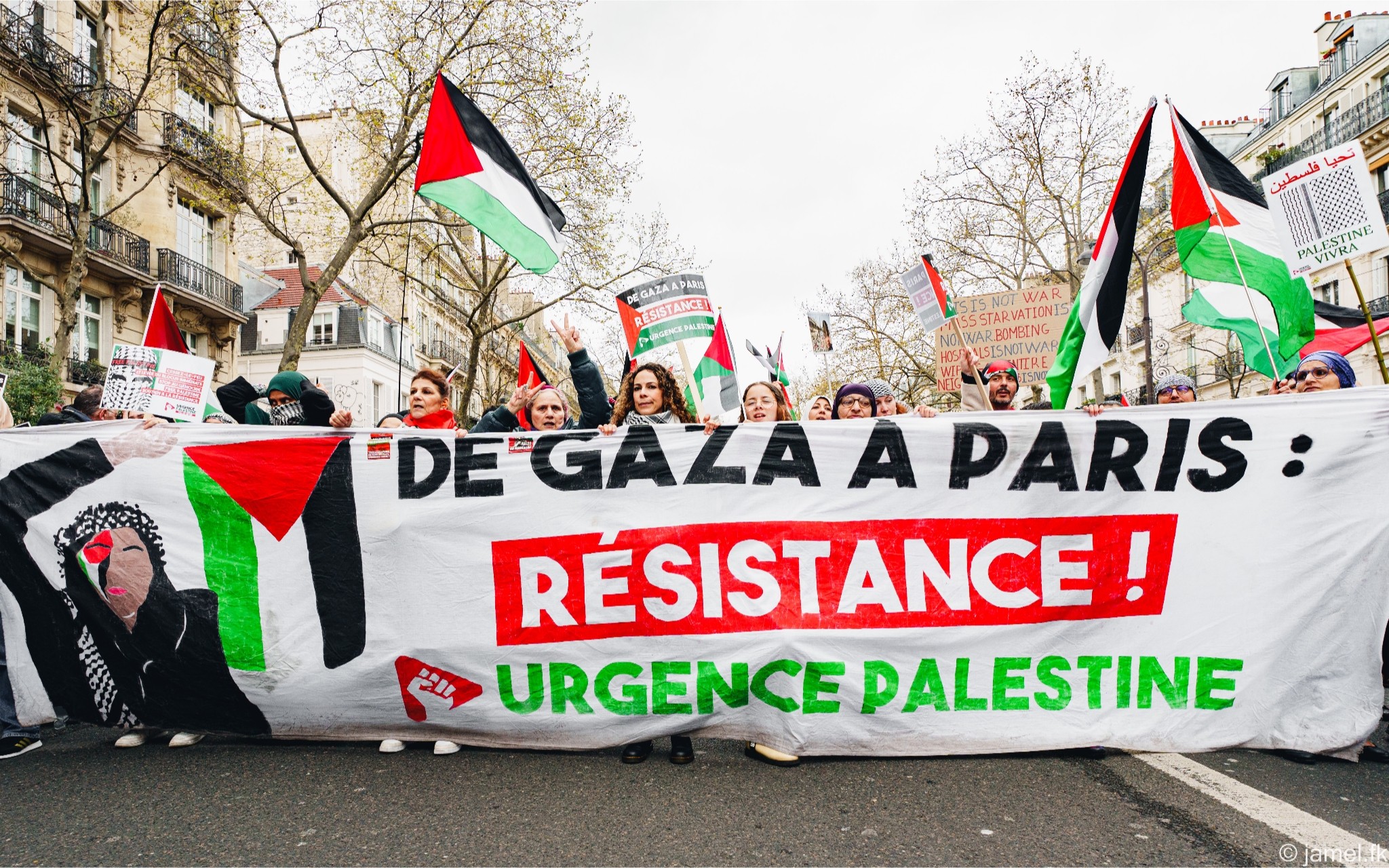 Manifestation du 30 mars 2024 à Paris : une foule derrière la banderole « De Gaza à Paris : Résistance ! Urgence Palestine », trois drapeaux palestiniens flottent. Photographie Jamel.fk.